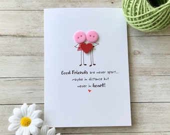 May include: A white card with two pink buttons representing people holding a red heart. The card reads "Good Friends are never apart... maybe in distance but never in heart!"