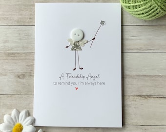 Op de afbeelding: Een witte kaart met een handgetekend plaatje van een vriendschapsengel met een witte knoop als hoofd en zilveren glittervleugels. De tekst luidt "Een vriendschapsengel om je eraan te herinneren dat ik altijd voor je klaar sta".