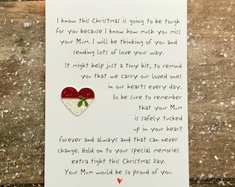 Op de afbeelding: Een witte kerstkaart met handgeschreven tekst, die troost en herinnering biedt. Een rood en wit hart met een groene tak is bevestigd. De kaart ligt op een houten oppervlak.
