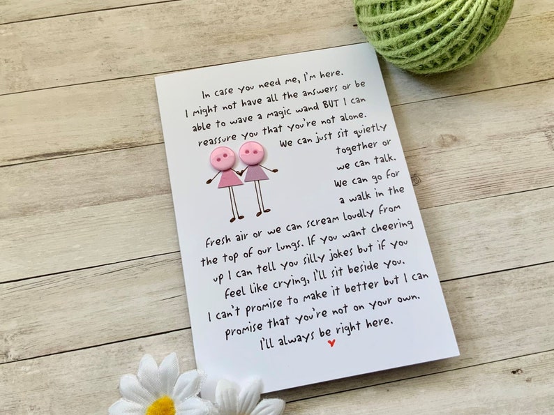 May include: A white card with pink buttons attached to it. The card has a handwritten message that reads: "In case you need me, I'm here. I might not have all the answers or be able to wave a magic wand BUT I can reassure you that you're not alone. We can just sit quietly together or we can talk. We can go for a walk in the fresh air or we can scream loudly from the top of our lungs. If you want cheering up I can tell you silly jokes but if you feel like crying, I'll sit beside you. I can't promise to make it better but I can promise that you're not on your own. I'll always be right here."