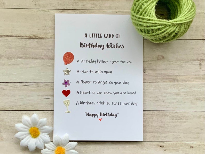 May include: A white card with the text "A Little Card of Birthday Wishes" and a list of birthday wishes with glitter embellishments. The wishes include a birthday balloon, a star, a flower, a heart, and a glass of wine.