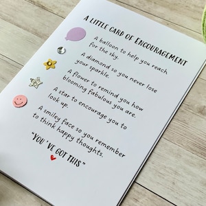 Op de afbeelding: Een witte kaart met de tekst "A LITTLE CARD OF ENCOURAGEMENT" en een lijst met bemoedigende zinnen. Elke zin wordt vergezeld door een klein, kleurrijk, decoratief element. De kaart bevat ook de tekst "YOU'VE GOT THIS" met een klein rood hartje.