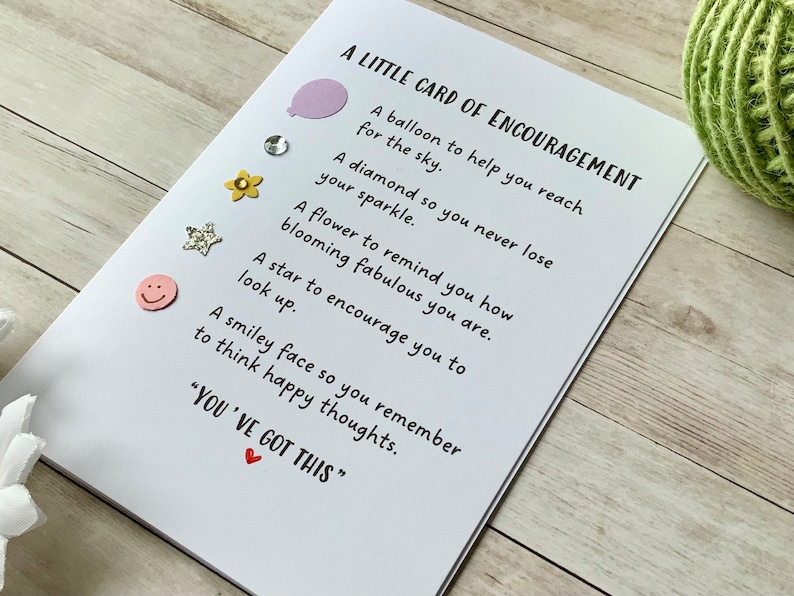 Op de afbeelding: Een witte kaart met de tekst "A LITTLE CARD OF ENCOURAGEMENT" en een lijst met bemoedigende zinnen. Elke zin wordt vergezeld door een klein, kleurrijk, decoratief element. De kaart bevat ook de tekst "YOU'VE GOT THIS" met een klein rood hartje.