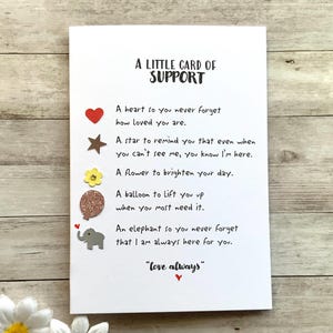 May include: A white card with the text "A LITTLE CARD OF SUPPORT" and a message with a heart, star, flower, balloon, and elephant. The card includes the phrase "love always".
