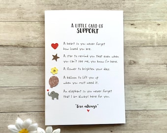 Op de afbeelding: Een witte kaart met de tekst "A LITTLE CARD OF SUPPORT" en een boodschap met een hart, ster, bloem, ballon en olifant. De kaart bevat de zin "love always".