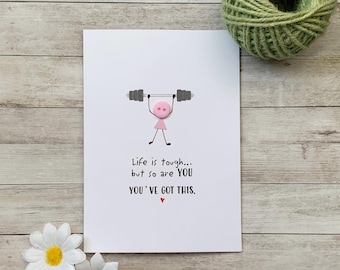 Op de afbeelding: Een witte kaart met een roze knoopfiguur die een halterstang van knopen optilt. De kaart luidt "Life is tough... but so are YOU YOU'VE GOT THIS."