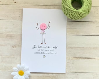 Op de afbeelding: Een witte kaart met een stokfiguurtekening van een persoon met een roze knoop als hoofd. De tekst op de kaart luidt "Ze geloofde dat ze het kon, dus ging ze ervoor en sloeg ze de spijker op de kop!"