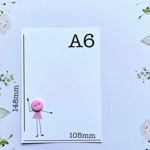 Pu&ograve; includere: Carta formato A6 con un bottone rosa e un disegno di un omino stilizzato. La carta misura 105 mm di larghezza e 148 mm di altezza.