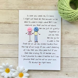 May include: A white card with a handwritten message about friendship and support. The message includes the text "In case you need me, I'm here." and "I'll always be right here." The card is decorated with two small buttons, one pink and one blue, representing two stick figures holding hands.