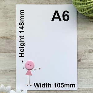 May include: A white A6 size paper with the dimensions of 148mm height and 105mm width. The paper has a pink button figure with arms and legs. The text "A6" is printed in black.