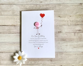 Op de afbeelding: Handgemaakte verjaardagskaart met een stokfiguur die een rode hartballon vasthoudt. De kaart heeft de tekst "On Your Birthday" en een boodschap van liefde en steun. Onderaan een witte madelief.