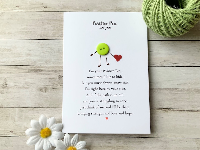 May include: A white card with a green button pea character holding a red heart. The card has a poem that reads "I'm your Positive Pea, sometimes I like to hide, but you must always know that I'm right here by your side. And if the path is up hill, and you're struggling to cope, just think of me and I'll be there, bringing strength and love and hope."