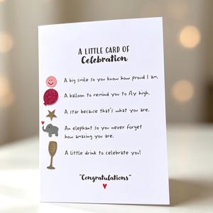 May include: A white greeting card titled A LITTLE CARD OF Celebration. It features a pink smiley face, a red glitter balloon, a gold star, a grey elephant, and a gold champagne flute icon, each paired with a line of text and ending with Congratulations.