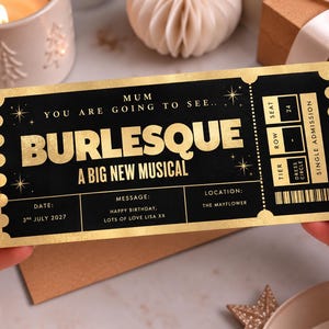 May include: A black and gold rectangular ticket with scalloped edges. The text reads: MUM YOU ARE GOING TO SEE.. BURLESQUE A BIG NEW MUSICAL. It includes fields for date 3rd July 2027, a birthday message, location The Mayflower, seat 24, and tier Dress Circle.