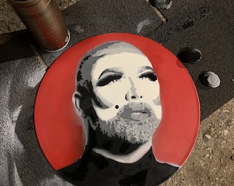 May include: A red vinyl record with a black and white stencil of a person's face. The person has a beard and is looking up.