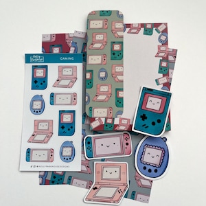 May include: Stationery set with a gaming theme, featuring illustrations of retro handheld consoles in pink, blue, and green. Includes stickers, notepaper, and a bookmark. The word "Gaming" is printed on one of the items.