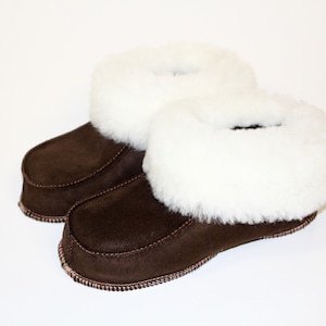 Peut inclure: Une paire de pantoufles en daim marron avec une doublure en peau de mouton blanche. Les pantoufles ont une pointe arrondie et une semelle plate.