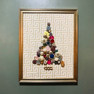 May include: A framed artwork featuring a Christmas tree made of colourful buttons and rhinestones on a white and gold patterned background.