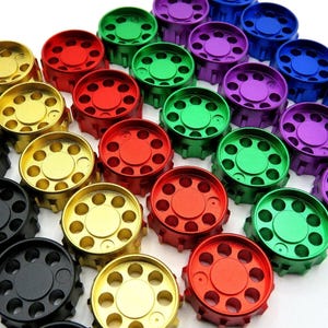 Puede incluir: Una colección de tapas metálicas de colores en una variedad de colores, incluyendo rojo, verde, dorado, negro y morado. Las tapas son de forma circular con múltiples agujeros alrededor del borde.