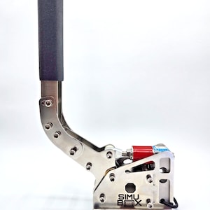 Op de afbeelding: Een zilveren handrem met een zwarte hendel en een rood onderdeel. De handrem is gemarkeerd met "SIMU BOX" in zwarte tekst.