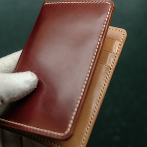 Peut inclure: Un portefeuille en cuir marron avec un int&eacute;rieur en cuir beige et des coutures blanches. Le portefeuille est ferm&eacute; et poss&egrave;de un rabat.
