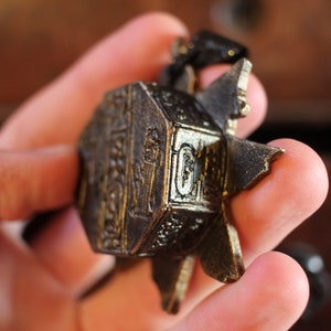 Puede incluir: Un colgante de metal dorado con detalles intrincados y un dise&ntilde;o en forma de estrella. El colgante se sostiene en una mano.