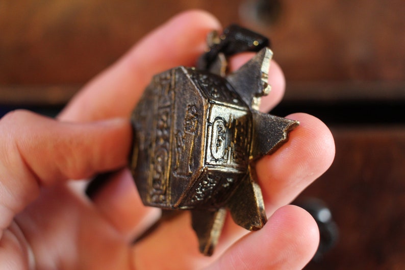 Puede incluir: Un colgante de metal dorado con detalles intrincados y un dise&ntilde;o en forma de estrella. El colgante se sostiene en una mano.