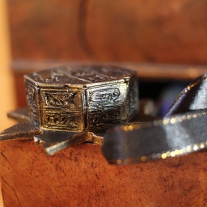 Puede incluir: Un adorno de estrella de metal dorado con una pieza central octogonal detallada y de m&uacute;ltiples capas. El adorno est&aacute; sobre una superficie de madera con una cinta negra.
