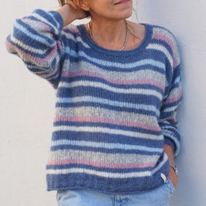 Könnte beinhalten: Ein gestreifter Pullover in Blau und Rosa mit langen Ärmeln und einem runden Ausschnitt.