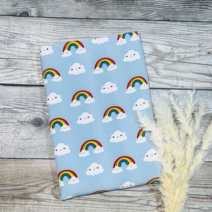 Könnte beinhalten: Ein hellblauer Stoff mit einem sich wiederholenden Muster aus bunten Regenbögen und weißen Wolken mit lächelnden Gesichtern.