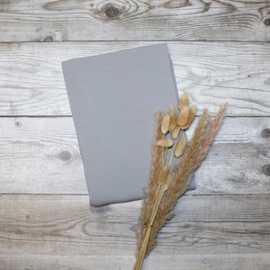 Könnte beinhalten: Ein graues Stoffrechteck auf einem Holzgrund mit einem Strauß getrockneter, beiger Pampasgräser.