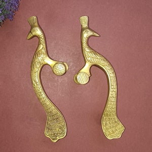 May include: Two gold peacock-shaped door handles with intricate details. The handles are made of brass and have a traditional design.