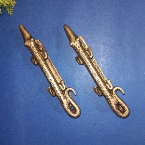 May include: Two gold-colored metal decorative hooks shaped like alligators. The hooks are detailed with scales and have a textured finish.