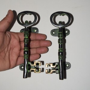 May include: Two black and green key-shaped door handles with brass accents. The handles are mounted on black metal plates with two screws each.