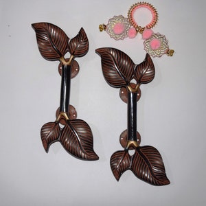 Könnte beinhalten: Zwei schwarze und braune, blattartige Türgriffe mit goldenen Akzenten. Die Griffe sind an runden Metallplatten befestigt.