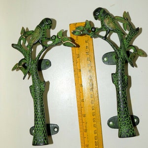 Puede incluir: Un par de tiradores de puerta de metal verde y dorado con forma de loros posados en ramas. Los tiradores miden aproximadamente 20 cm de largo.