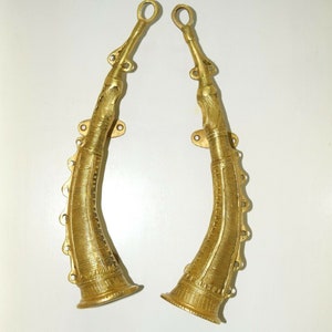 Può includere: Un paio di maniglie per porte in metallo dorato a forma di corna con disegni intricati. Le maniglie sono fissate a una parete.