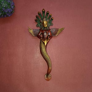 May include: A gold, green and red metal door handle shaped like a snake with a human figure on top. The figure has wings and a halo.