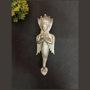 May include: Silver door handle featuring an intricate design of a woman with wings and a snake crown. The woman is in a prayer position with her hands clasped together.