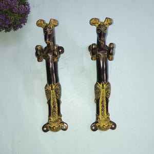 May include: A pair of ornate brass door handles shaped like stylised animals with intricate details. The handles are dark brown with gold accents.
