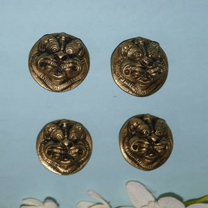 Può includere: Quattro bottoni in metallo color oro con un designo dettagliato di un viso di leone. I bottoni sono rotondi e hanno un design in rilievo.