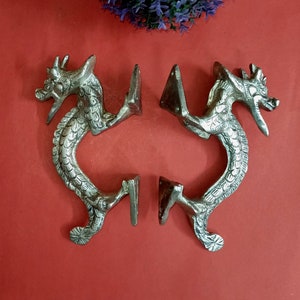 Könnte beinhalten: Ein Paar silberne Drachentürgriffe mit filigranen Details. Die Griffe sind an einer Metallplatte mit einem dekorativen Design befestigt.