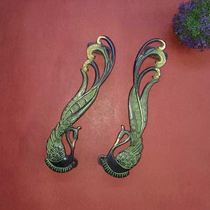 Może przedstawiać: Para ozdobnych klamki drzwiowych w kształcie pawia. Klamki są wykonane z mosiądzu i mają czarny i zielony kolor.