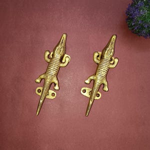 May include: Two gold crocodile door handles with a textured finish. The handles are mounted on a flat surface.