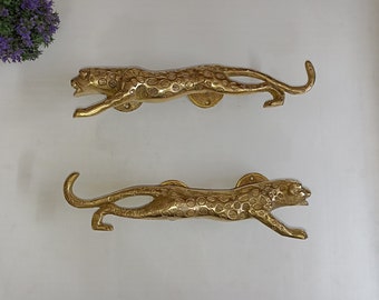 May include: Two gold-toned door handles shaped like leopards. The handles are detailed with a leopard print pattern.