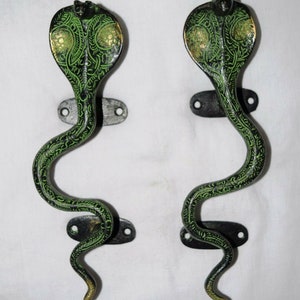 Puede incluir: Un par de tiradores de puerta decorativos con forma de cobras verdes con detalles en negro y dorado. Los tiradores son de metal y tienen un diseño tradicional.