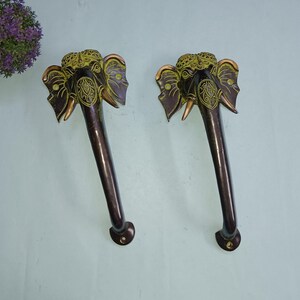 Könnte beinhalten: Ein Paar antike Messing-Türgriffe mit Elefantenkopf-Designs. Die Griffe sind dunkelbraun mit goldenen Akzenten und aufwendigen Details.