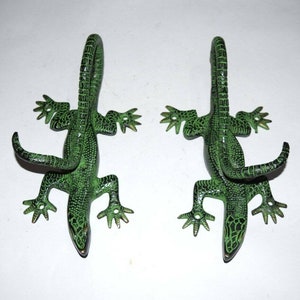 May include: Two green metal lizard hooks with curled tails. The hooks are designed to look like lizards with detailed scales and claws.