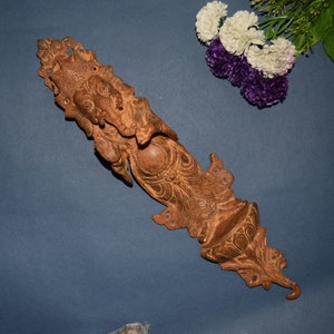 Może przedstawiać: Szczegółowa, misterna, drewniana klamka do drzwi z przedstawieniem hinduskiego bóstwa Ganesha. Klamka ma bogaty brązowy kolor i rustykalny, antyczny wygląd.