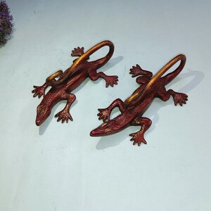 May include: Two red and gold metal lizard wall hooks. The lizards are curled up with their tails forming a hook.